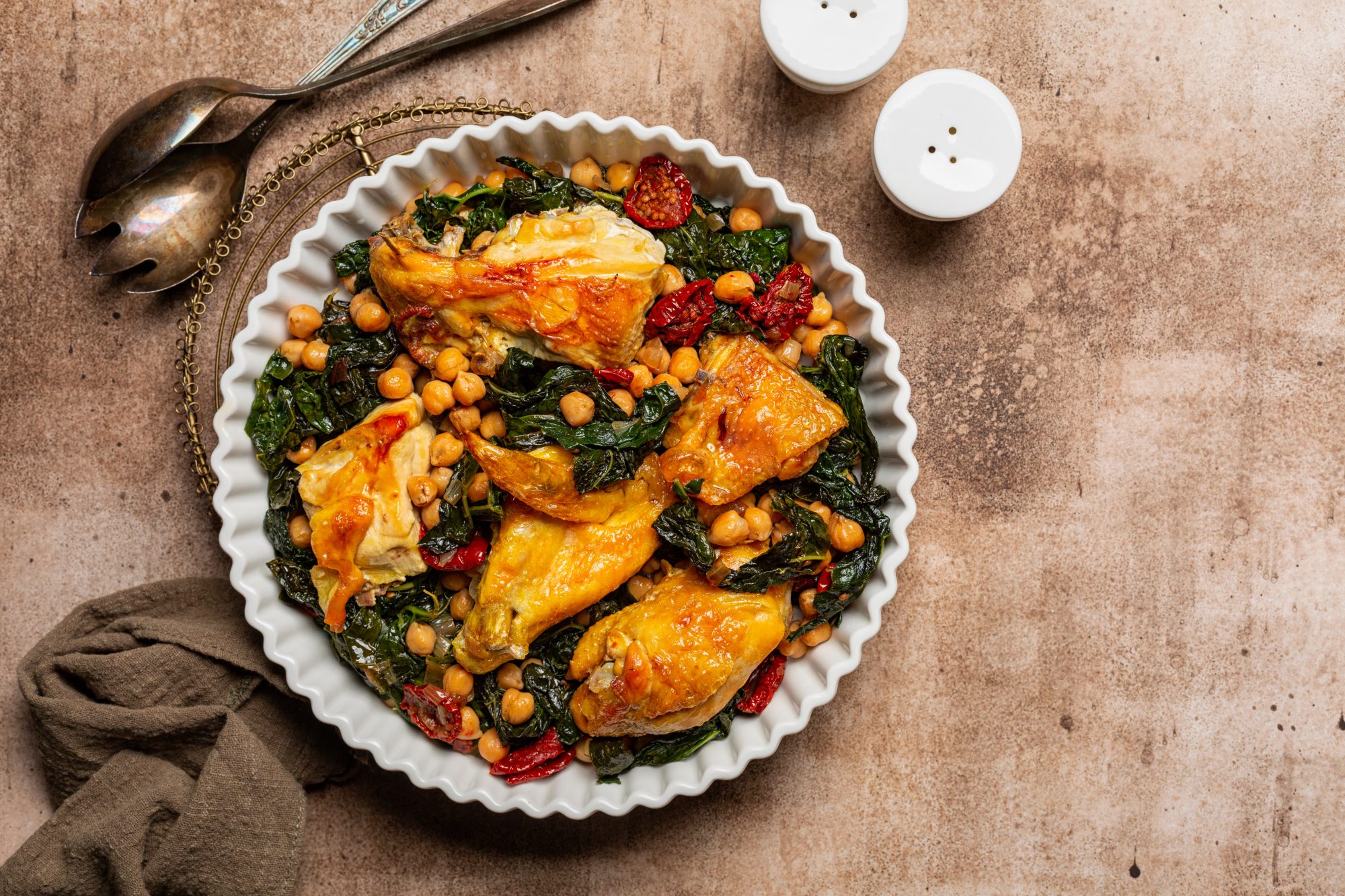 chicken with kale, chickpeas and sun-dried tomatoes. Top view. Copy space, brown table surface.