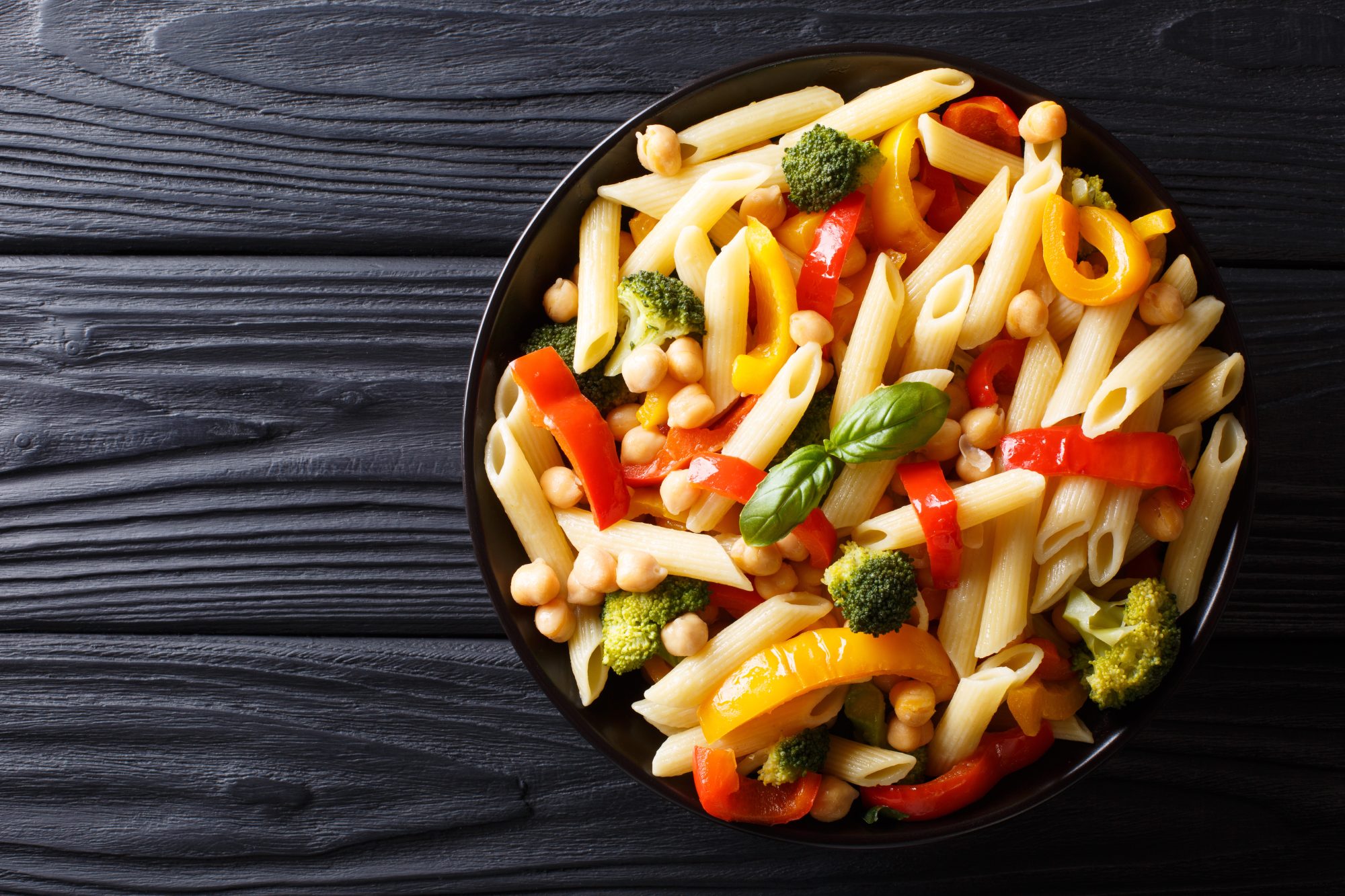 Penne pasta with chickpeas, broccoli, bell pepper and spices close-up in a plate. horizontal top view